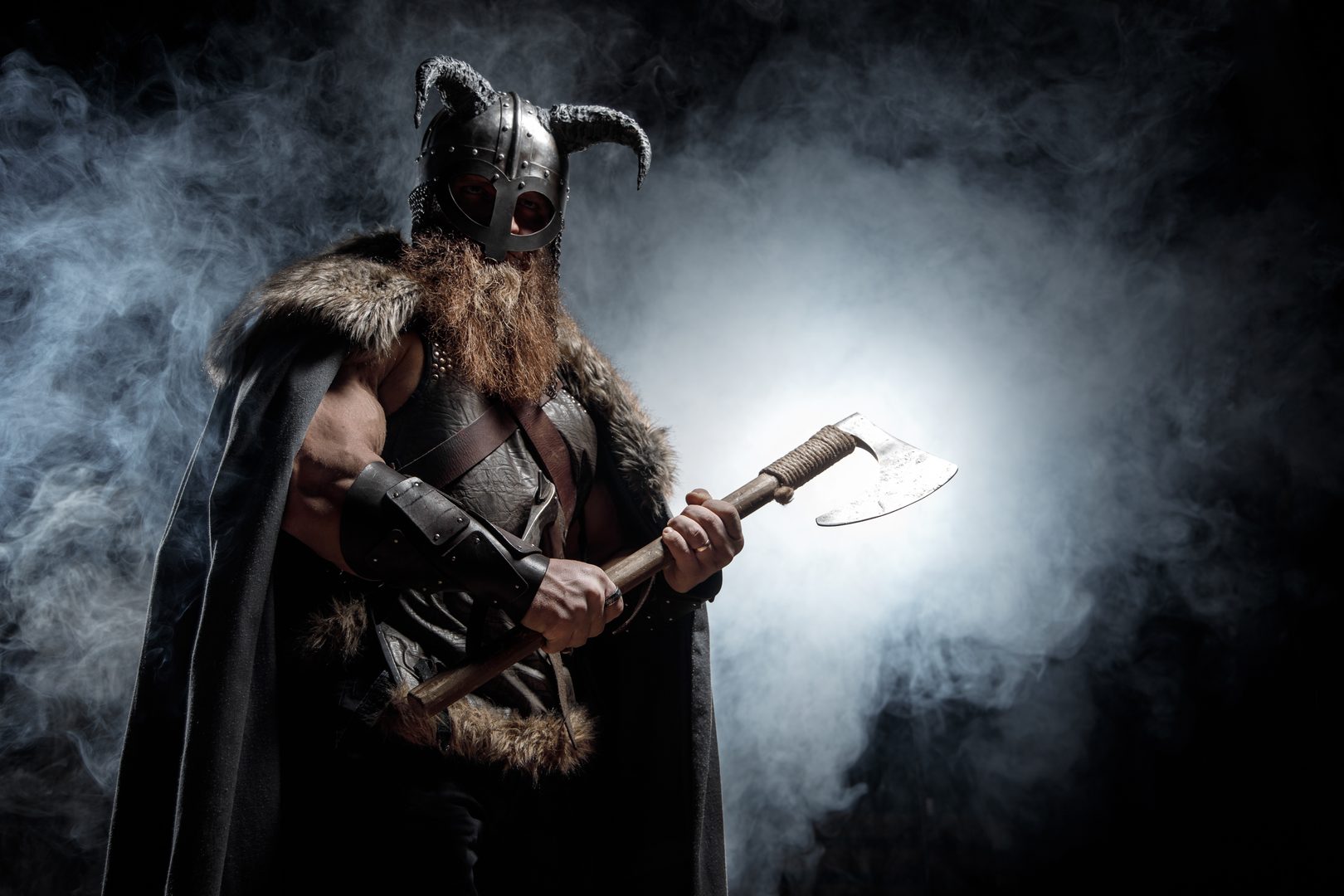 A Viking warrior in full armor holding an axe in dramatic smoke