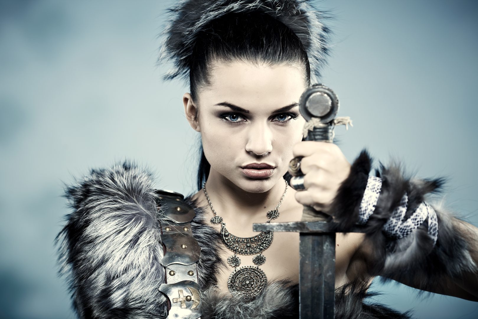 A dark-haired warrior woman holding a sword at eye level, cold and focused
